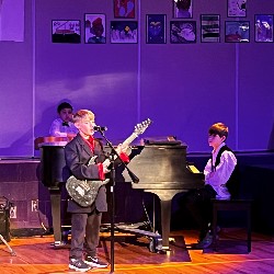 Three TDVA students perform music on stage.